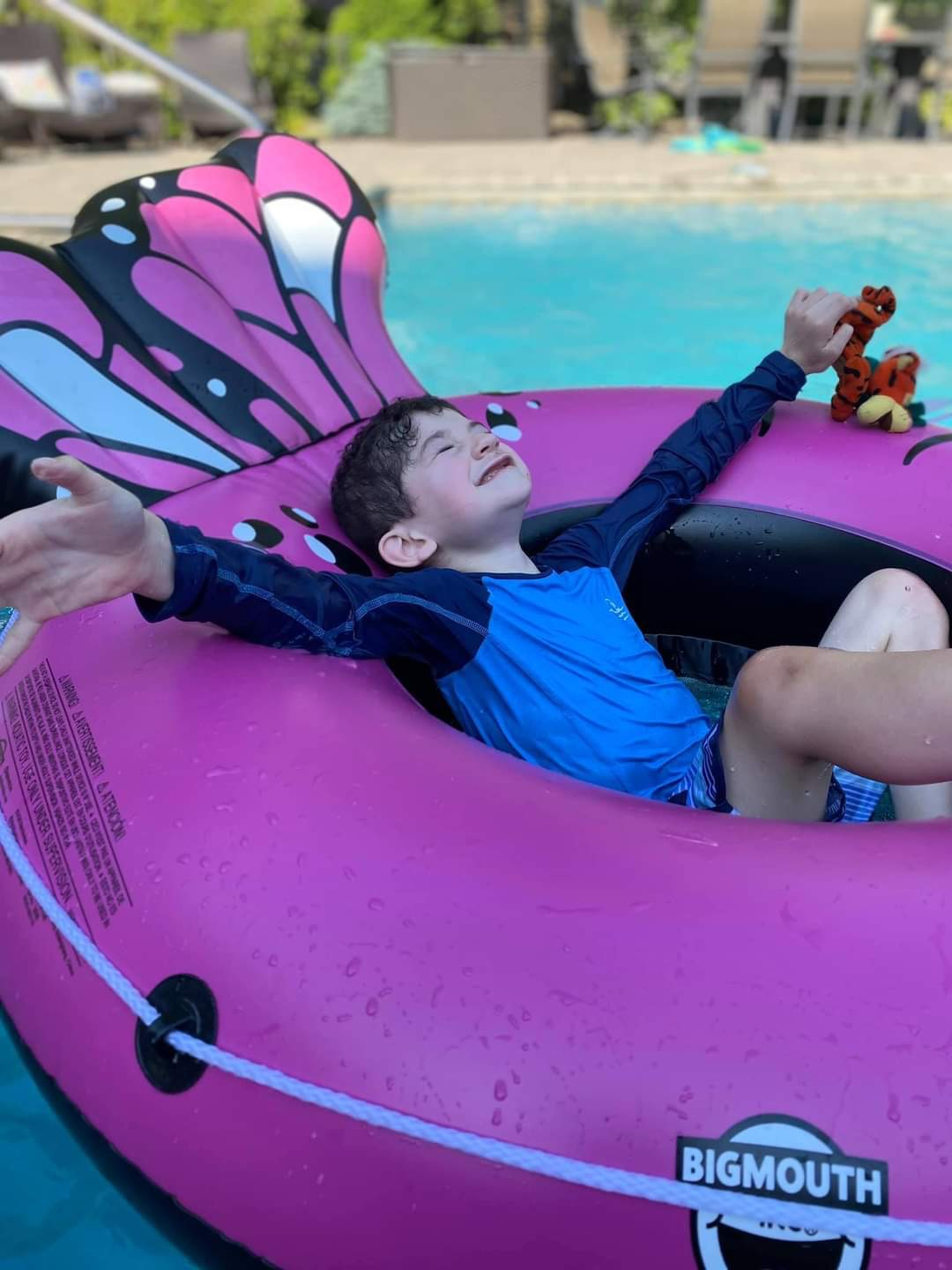 Dylan smiling on a bright pink pool float